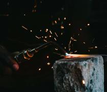 A student holding a welding torch creates sparks on a piece of steel.