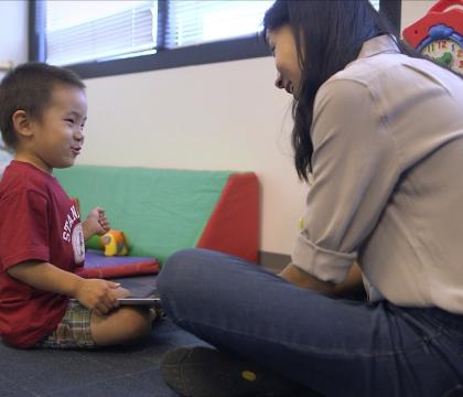 Woman sits across from smiling child in red Stanford shirt